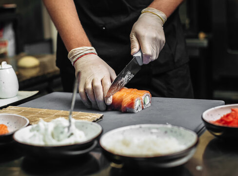 Chef coock cut fresh sushi rolls with sharp knife on the cutting board in restaurant. hands close up
