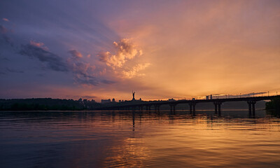 Orange blue sunset on the Dnieper river in Kyiv. Panorama of the bridge. Clouds in the sky.