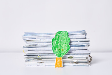 a green leaf on top of some newspaper stacked in front of each other papers and a tree.