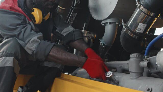 Hardworking African American mechanic using bolt wrench while repairing pipelayer machine at plant