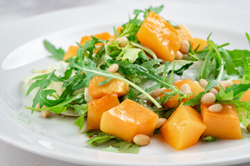 Italian vegetarian salad of baked pumpkin with pine nuts, arugula and cheese. Bright fresh salad with pumpkin slices, close up