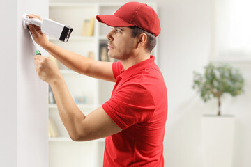 Young man installing a security camera on a wall in a room