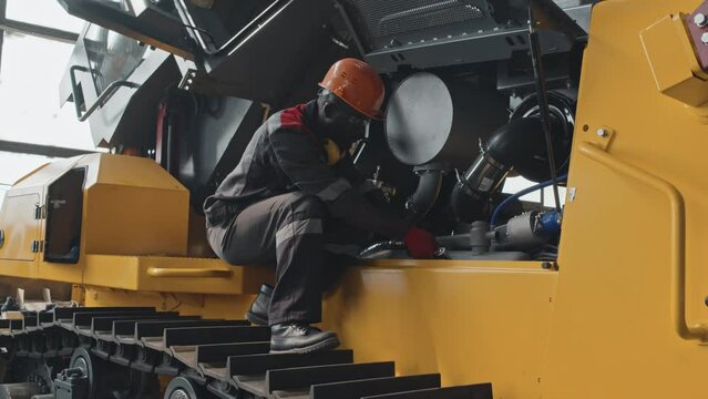 African American male mechanic worker using bolt wrench while repairing bulldozer at service centre