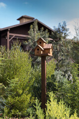 Handmade triple birdhouse on a wooden tall stand against a blurred cottage.
