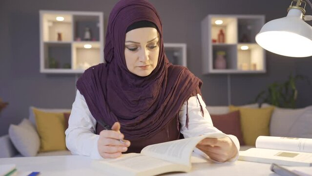 Muslim female student wearing hijab is studying for her lessons.
A Muslim female university student wearing a headscarf at home.
