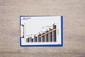 a bar chart on a clipboard with a pen in the middle and an arrow pointing upward at the top