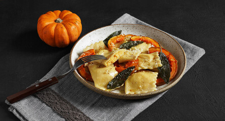 Homemade Pumpkin Ravioli with ricotta cheese served sage butter and hard cheese on plate on black table with small pumpkin. selective focus