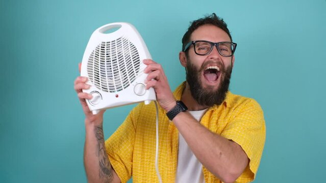 A cheerful handsome hipster guy with a beard in glasses and casual clothes presents, advertises an electronic fan heater. The concept of problems with gas in Europe. Alternative heating.