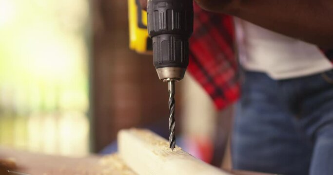 African American female carpenter using drill machine on wood. Woman drills a tree with a drill.