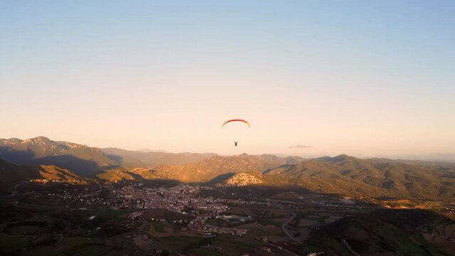 Aerial shot following a Paraglider flying above the Countryside at sunset