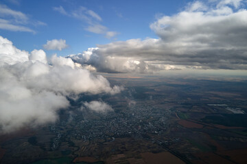 Aerial view from airplane window at high altitude of distant city covered with puffy cumulus clouds forming before rainstorm