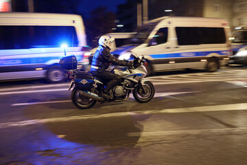 Policjant wydziału ruchu drogowego z motocyklem podczas kontroli miasta wieczorem.  Światła policyjne. - obrazy, fototapety, plakaty