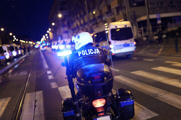 Policjant wydziału ruchu drogowego z motocyklem podczas kontroli miasta wieczorem.  Światła policyjne. - obrazy, fototapety, plakaty