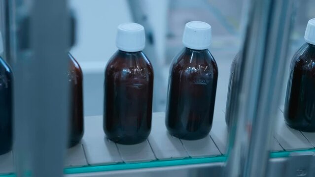 Industrial line of food, medical or chemical industry for filling liquids into glass or plastic brown transparent bottles with white caps. Closeup