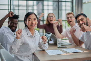 group of different business people celebrating victory while sitting at table in modern office