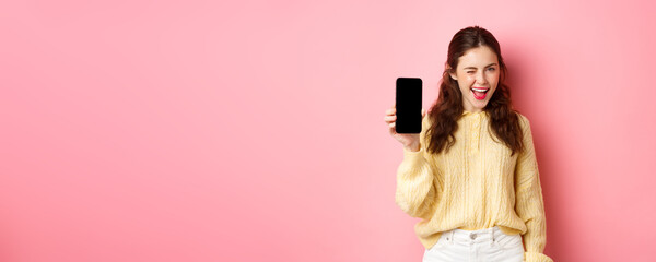 Image of cheeky attractive girl, showing you smartphone screen, winking and smiling, recommending...