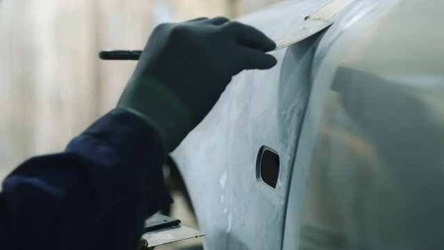 Car body repair. Mechanic apply putty on the car body with a spatula.