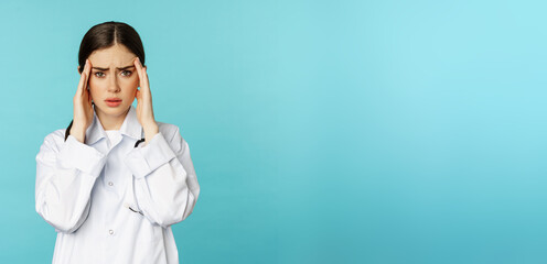 Image of woman doctor, medical personel grimacing from discomfort, having headache, migraine, feeling deezy, standing over torquoise background - obrazy, fototapety, plakaty