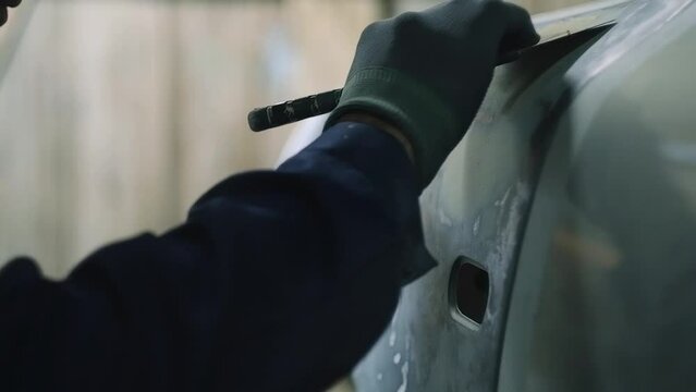 Car body repair. Mechanic apply putty on the car body with a spatula.