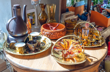 Close-up of vintage brown glassware on metal utensils. Carved bowl made of wood with a pattern. Wooden table. Sunlight.