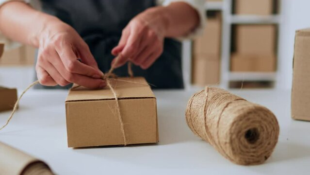 A packer in a warehouse is tying up a gift for a customer. craft paper packaging by warehouse worker, e-commerce online store, shipping goods, brown boxes for goods
