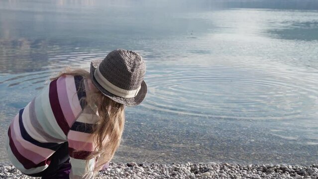 Kid throwing rocks across water at sea beach. Child skipping stones on lake surface. Girl playing, enjoying holidays on nature. Concept of mindfulness, mental health, digital detox. Lifestyle moment
