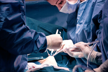 Surgeon and his assistant performing cosmetic surgery in hospital operating room. Surgeon in mask wearing loupes during medical procadure. Breast augmentation, enlargement, enhancement, breast cancer