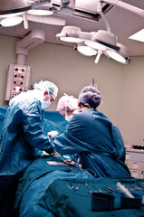 Surgeon and his assistant performing cosmetic surgery in hospital operating room. Surgeon in mask wearing loupes during medical procadure. Breast augmentation, enlargement, enhancement, breast cancer