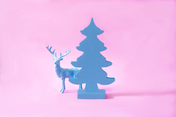 A blue reindeer behind a plain blue Christmas tree on pink background. Surreal minimal creative...
