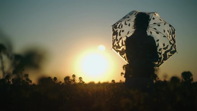 shot of a women twirling the umbrella in a flowering rape field at the sunset
