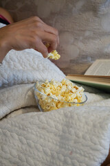 mature woman eating popcorn on sofa reading old book wearing bracelet pillow comfortable relaxing book read eat movie butter popcorn retired enjoying winter cold living room home life style interior 