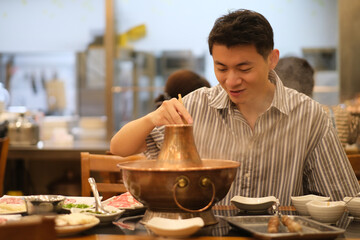 smiling Chinese young man eating Instant-boiled mutton hot pot in restaurant, a traditional Chinese...