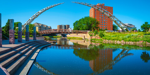 Big Sioux River public park riverfront trail landscape with water reflections of the bridges in downtown Sioux Falls, South Dakota, USA