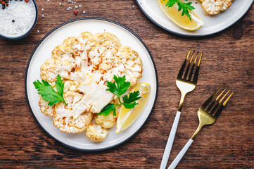 Baked cauliflower steak on plate, rustic wooden table background, top view