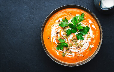 Hot spicy pumpkin soup puree with pumpkin seeds, cream, pepper and parsley. Winter or autumn healthy vegan vegetarian food. Soup bowl on black table background. Top view
