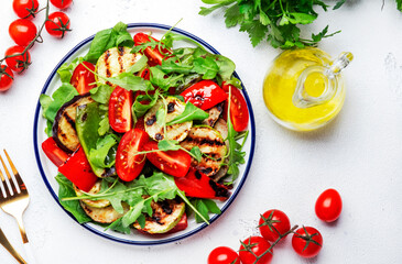 Healthy vegan salad with grilled vegetables, paprika, zucchini, eggplant with fresh tomatoes and mixed herbs. White table background, top view