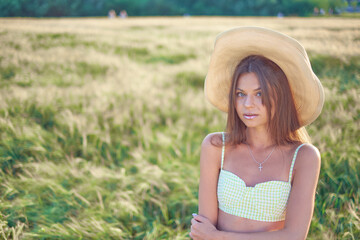 Obraz premium stylish beautiful smiling young girl in a straw hat and a fashionable dress walks around the field and poses