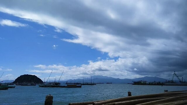 Timelapse video. sea view during the day. clouds moving towards the east. mountains and islands in the background. fishing boats leaning against.