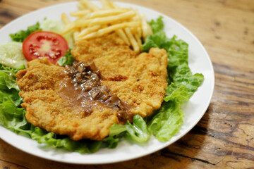 Chicken schnitzel served with mushroom sauce, french fries, lettuce, cucumber and tomato pieces