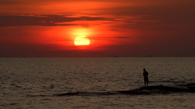 Sunset seascape with silhouette fishing man with dark and warm lighting in 4K footage.