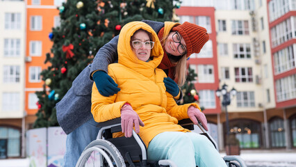 Caucasian woman driving her friend in a wheelchair by the Christmas tree.