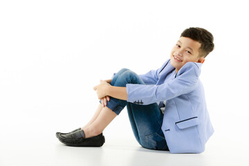 A 10-year-old Asian boy in a casual jacket is sitting on the ground, hands on his knees and smiling cheerfully, looking at the camera. - 545336299