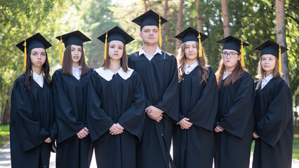 Seven graduates in robes stand in a row outdoors.