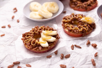 Creative party snack for holidays. Apple rounds with peanut butter, caramel and chocolate flavor puffed rice topping with banana slices. Funny appetizer for kids and adults.