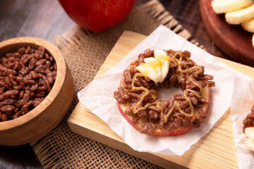Creative party snack for holidays. Apple rounds with peanut butter, caramel and chocolate flavor puffed rice topping with banana slices. Funny appetizer for kids and adults.