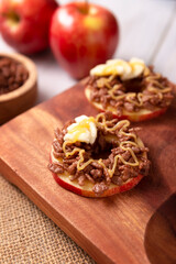 Creative party snack for holidays. Apple rounds with peanut butter, caramel and chocolate flavor puffed rice topping with banana slices. Funny appetizer for kids and adults.