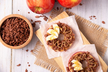Fototapeta premium Creative party snack for holidays. Apple rounds with peanut butter, caramel and chocolate flavor puffed rice topping with banana slices. Funny appetizer for kids and adults.