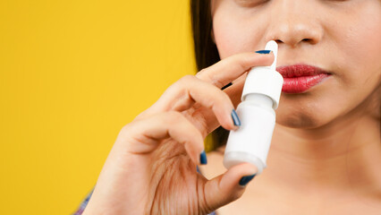 Sick unhealthy ill allergic young woman holding nasal drops or nose drop bottle isolated over yellow background