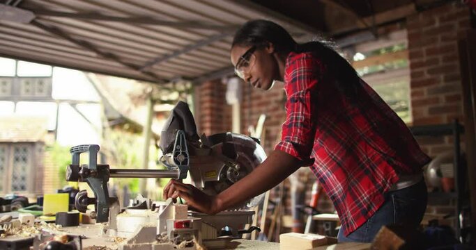 African American female carpenter cutting wooden plank with a circular electric saw in carpentry workshop