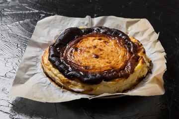 Spanish Basque cheesecake on parchment paper, on black slate, closeup